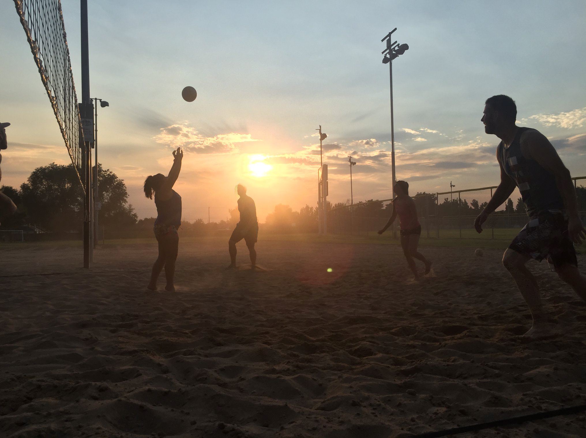lively sand volleyball game at sunset, with players in action, a volleyball mid-air.
